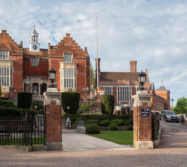 A large historic church building with pointed arch windows and a central entrance, situated in a landscaped area flanked by blooming cherry blossom trees with pink and white flowers. The building feat
